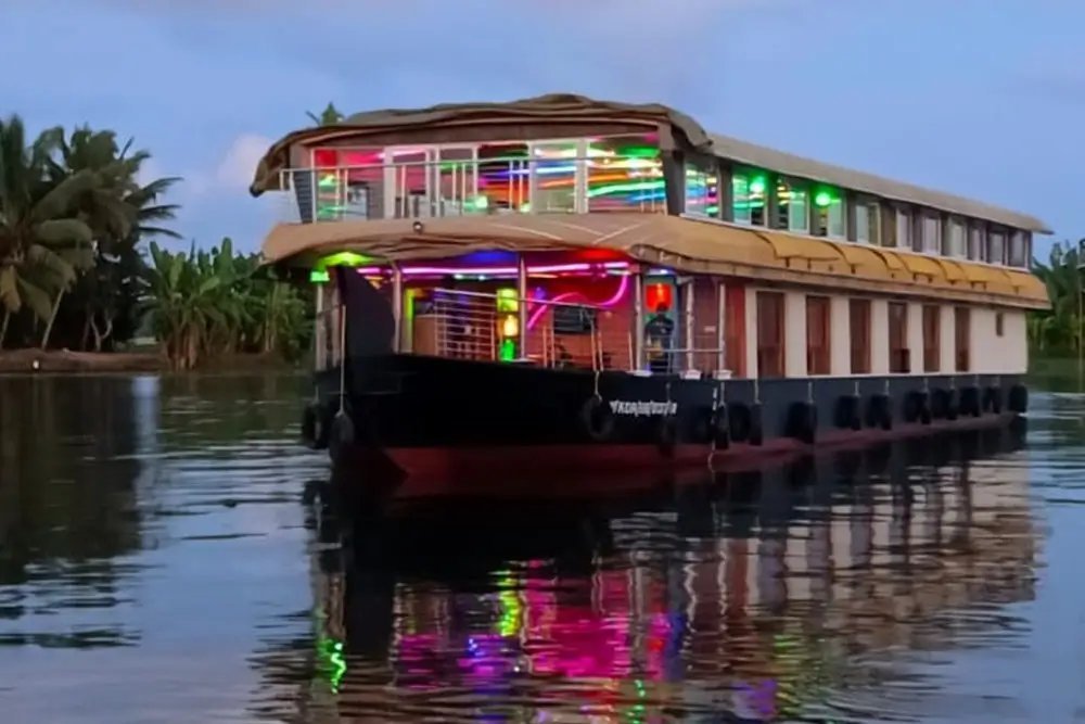 Kalarcode Kaliyodam deluxe 8 bedroom double-deck houseboat lit with colourful lights at dusk