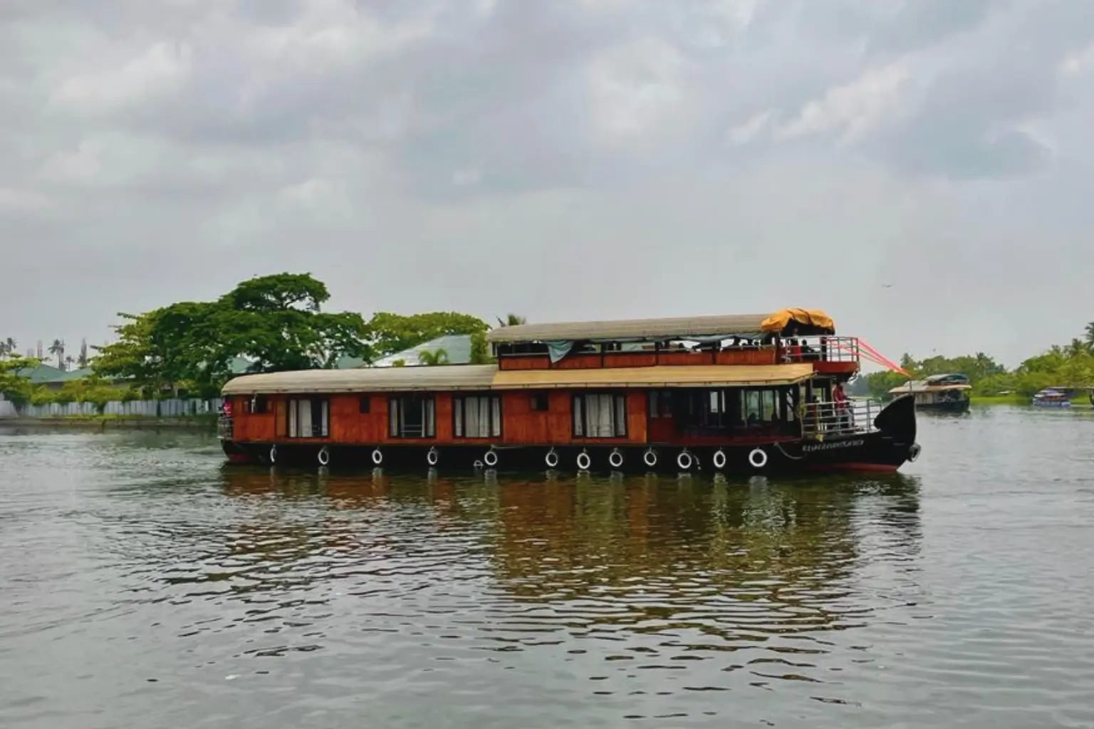 Thalavady Tharangam deluxe 4 bedroom houseboat on wide still water under a cloudy sky
